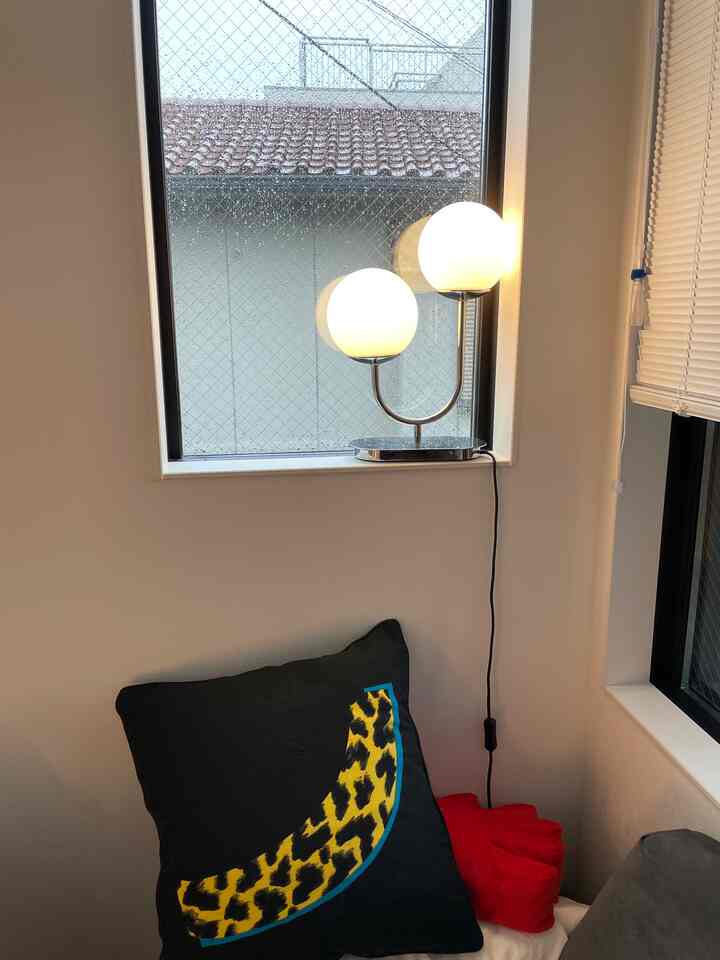 ホワイトの壁と窓枠のある照明が灯るコーナースペース、黒いクッションと赤い小物がポイントのシンプルなインテリア