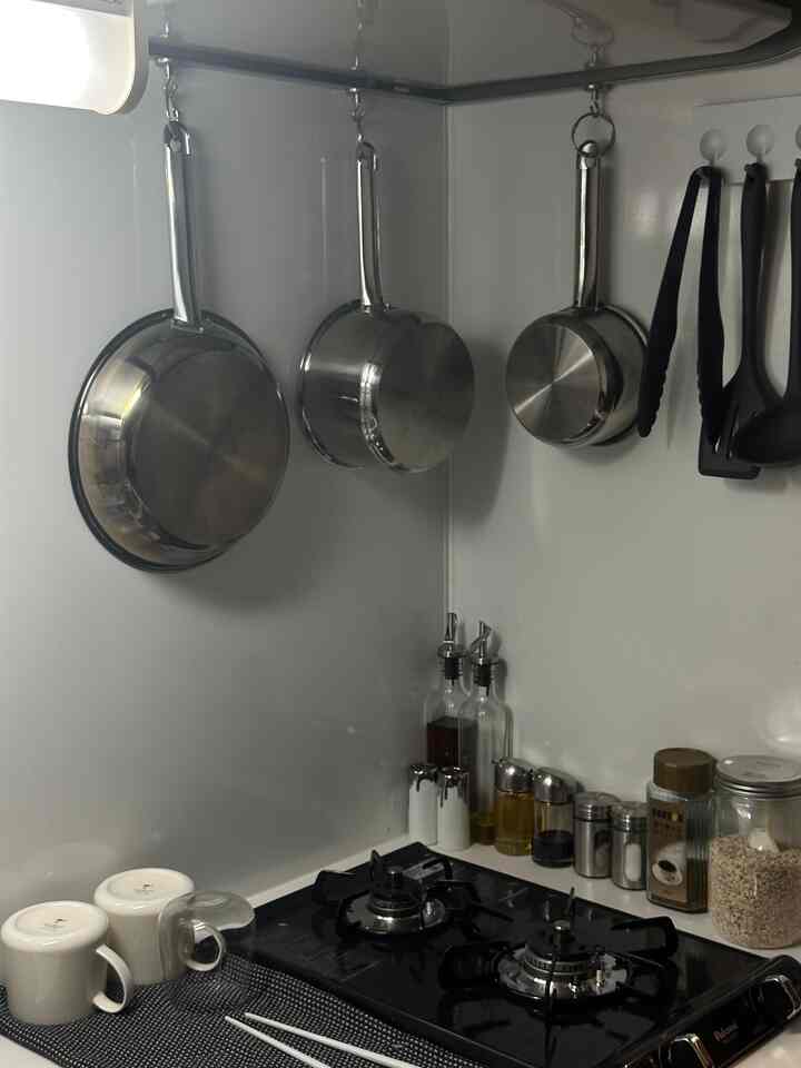A sleek kitchen with silver metal pots and utensils hanging on the wall, white mugs and chopsticks placed over a black gas stove