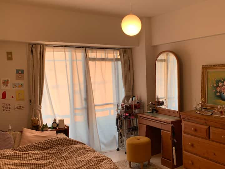Cozy bedroom with warm beige and wood tones, featuring curtains by the window and a vanity with mirror