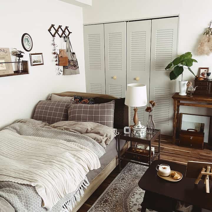 ベージュと木目調が調和した暖かみのある寝室、ナイトテーブルのテーブルランプとレトロな壁掛けフックが印象的なインテリア