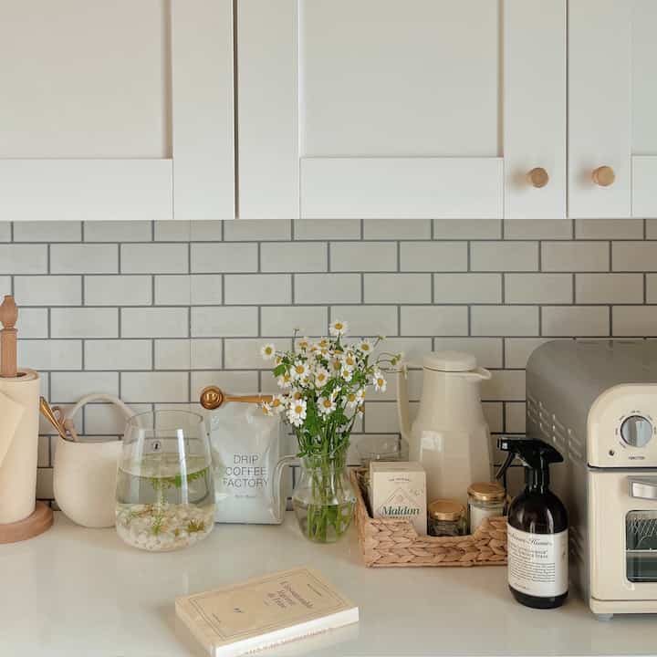 白を基調としたキッチン、中央に花瓶とコーヒー用品が配置された清潔で落ち着いた雰囲気のインテリア