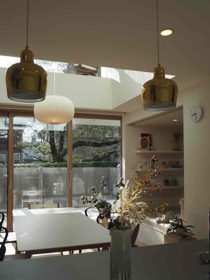 Bright white and natural tone dining room featuring gold pendant lights and large windows creating a cozy atmosphere