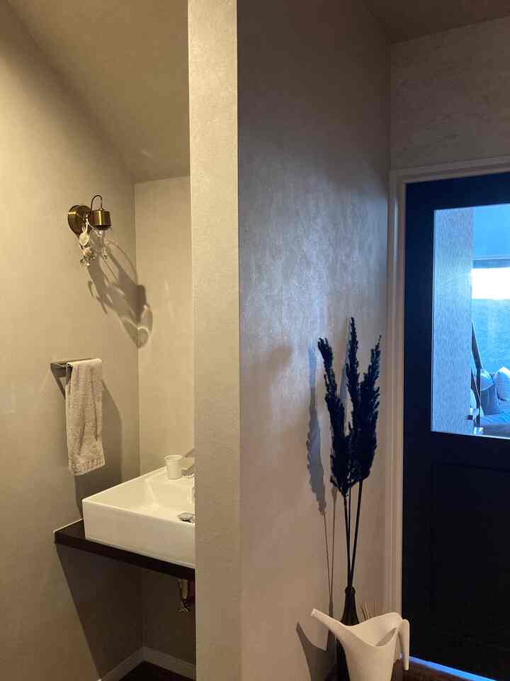 温かみのあるブラウンとホワイトの玄関とお手洗い、壁付け照明と洗練された手洗い器が配置された雰囲気のあるインテリア