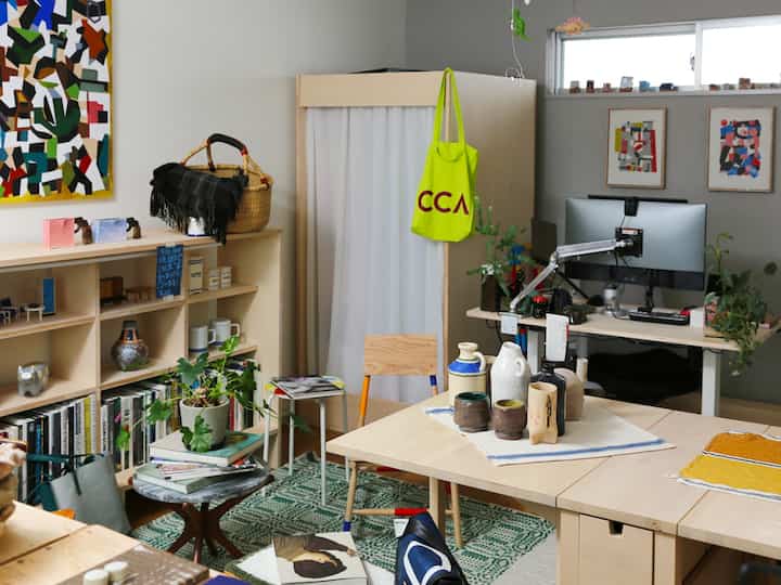 ナチュラルな色調のワンルーム作業空間、木製家具と本棚が配置され、テーブルに陶器作品が展示された雰囲気のあるインテリア