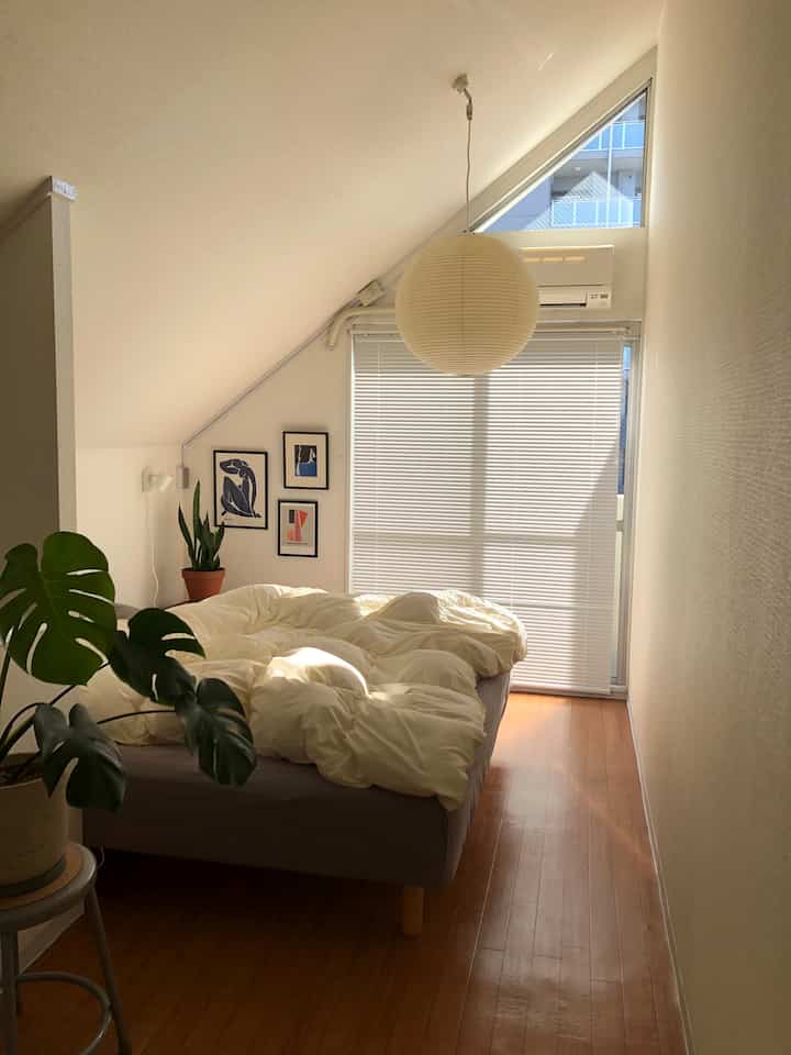 ベージュと白を基調とした狭い寝室、大きなベッドとポスター、植物が配置された自然な雰囲気のインテリア