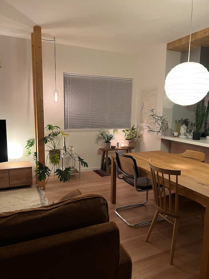 白い壁と木目調家具、多様な植物と照明が配置されたナチュラルな雰囲気のリビング・ダイニング空間