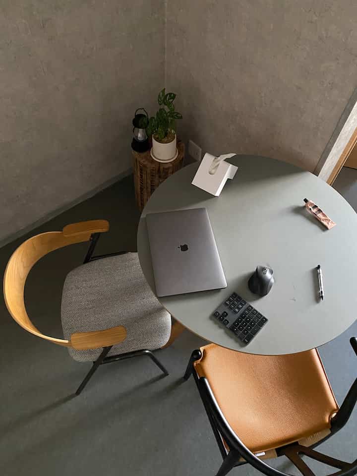 グレーとナチュラルカラーが調和した小さなワンルームのホームオフィス、丸テーブルと個性的な椅子が印象的なミニマルな空間