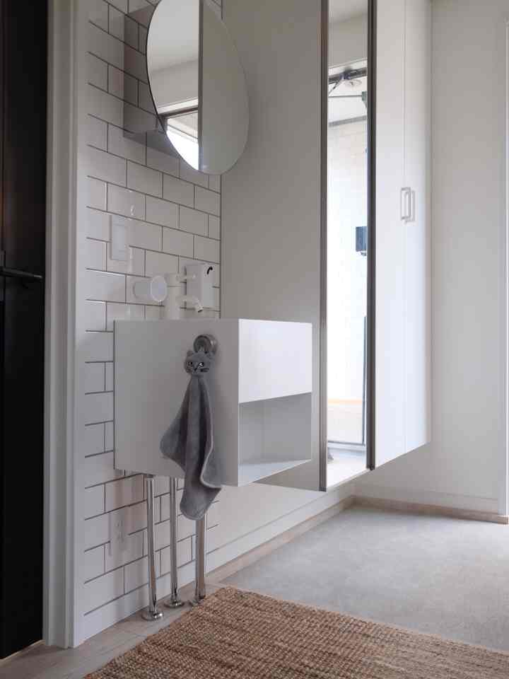 白と茶色のトーンの玄関、手洗いシンクと猫の形のタオル、編みラグが配置された印象的な空間