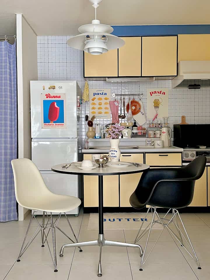 黄色を基調としたキッチン、丸いダイニングテーブルに2脚の椅子と中央にペンダントライトが配置された雰囲気のある空間