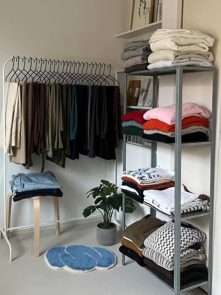 Natural color tone small room featuring single household clothes rack and metal shelves with neatly folded clothing, creating organized storage space
