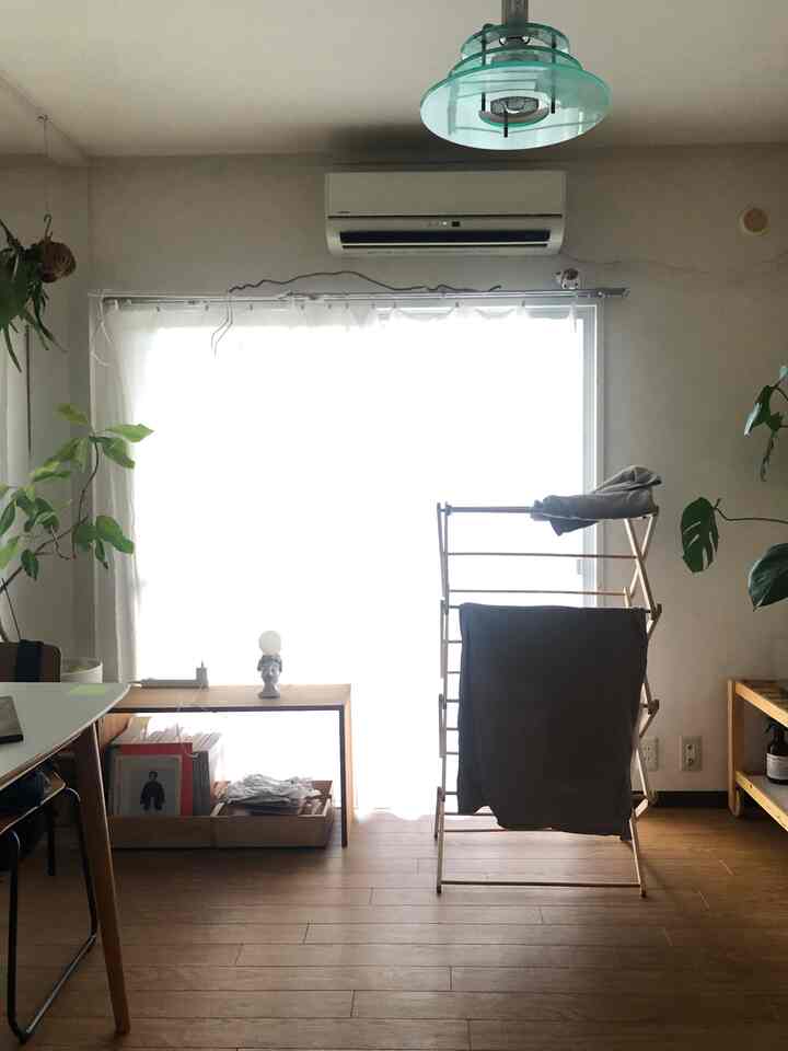 Natural wood-tone floor and bright balcony window with a clothes drying rack centrally placed in a neat living space