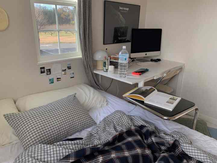 白色のトーンが印象的な寝室、チェック柄の寝具とコンピュータのあるデスクが配置された雰囲気のある空間