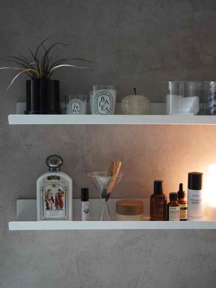 Gray wall bathroom space featuring white shelves neatly arranged with aroma candles and skincare products in a modern interior