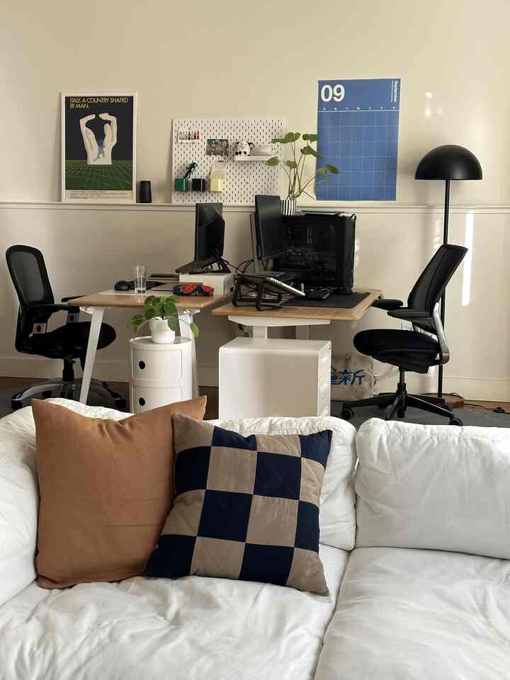 A white and wood tone home office featuring sofa, desks, and a floor lamp with a warm atmosphere