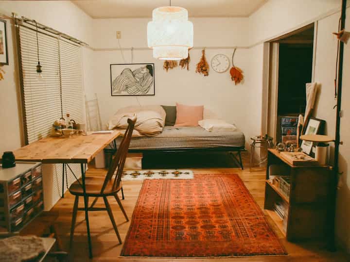 Natural tone living room featuring a sofa bed, wooden desk, and warm lighting with cozy atmosphere