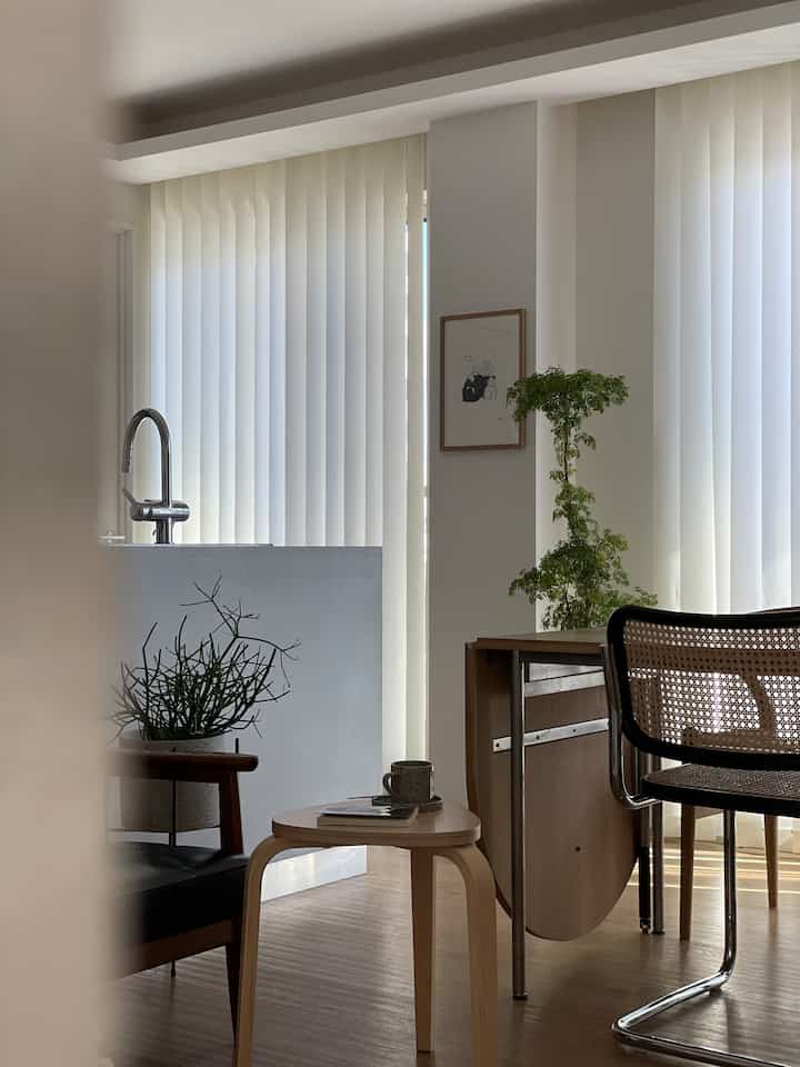 白とナチュラルカラーのリビングダイニング、木製のダイニングテーブルと落ち着いたアームチェア、植物が配置されたモダンな雰囲気のインテリア