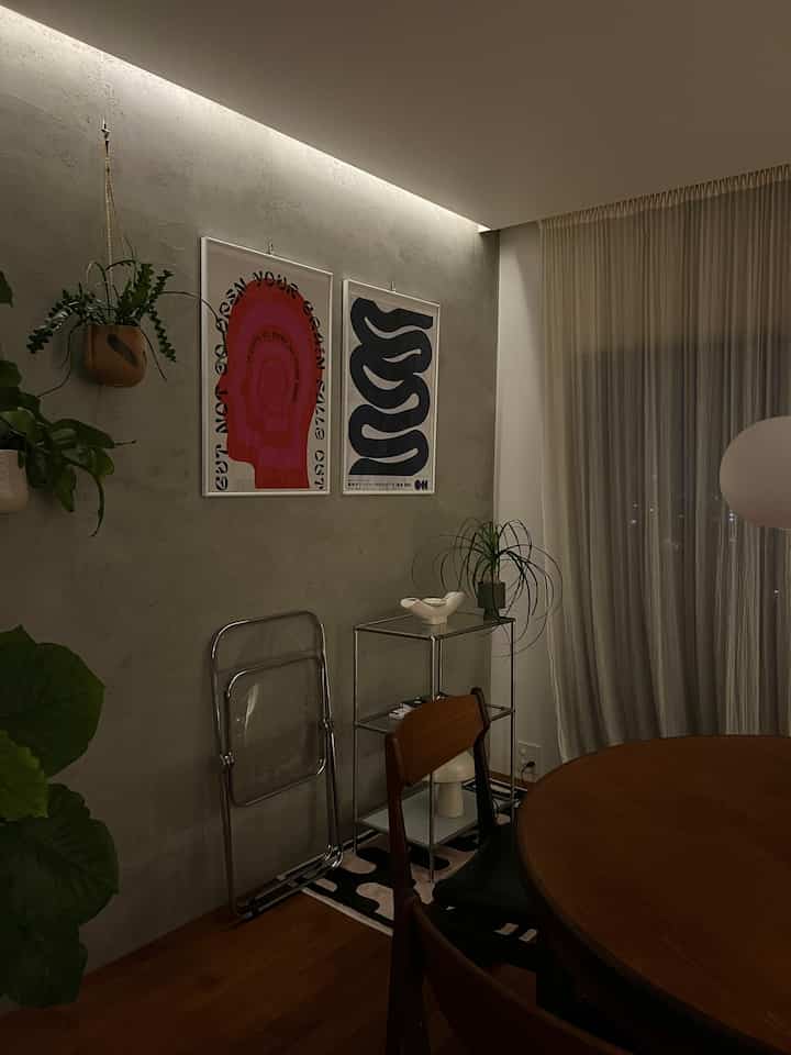 暗いトーンのリビングルーム、木製ダイニングテーブルと椅子、植物とメタルのサイドテーブルが配置された落ち着いた雰囲気のインテリア