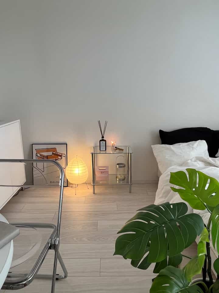 白とナチュラルカラーが調和した寝室、透明な椅子とガラスのサイドテーブル上にディフューザーが置かれた雰囲気のあるインテリア