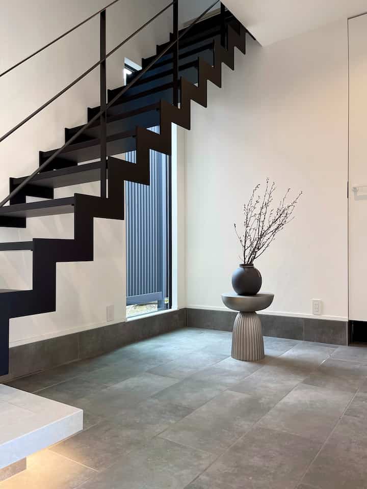 ホワイトの壁とライトグレーのタイル床、モダンな黒い階段と植物の入ったシンプルな空間