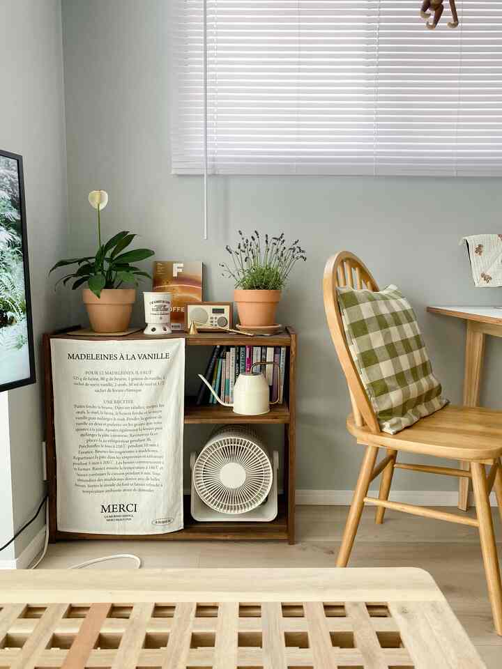 柔らかな薄緑色の壁とブラインドがあるナチュラルスタイルのコンパクトなリビング、木製家具と植物が配置された居心地の良い空間