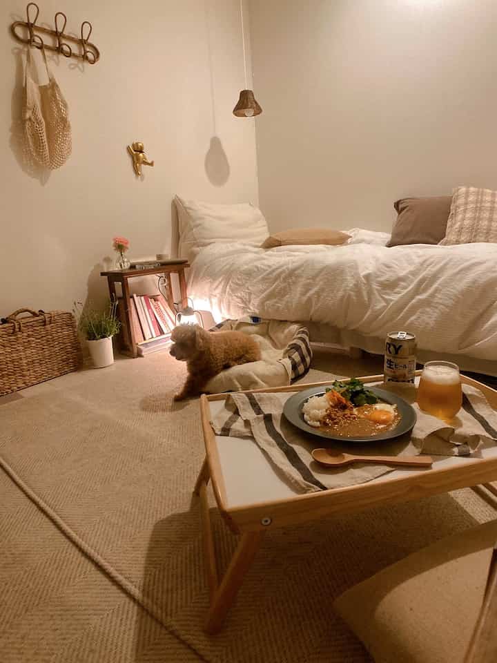 ナチュラルトーンの一人暮らし用寝室、ベッド横に小さなトレイテーブルと犬のベッドが配置された温かみのある空間