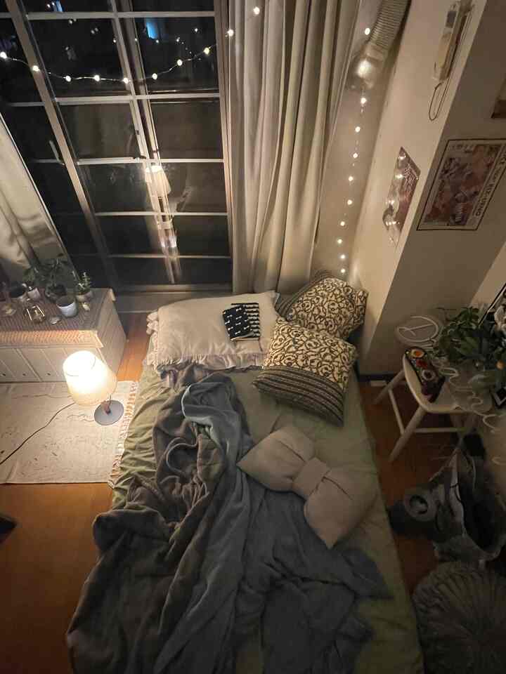 暖かい木目調とナチュラルな色合いの落ち着いた寝室、ベッド、テーブルランプ、ストリングライトが調和した雰囲気のあるインテリア