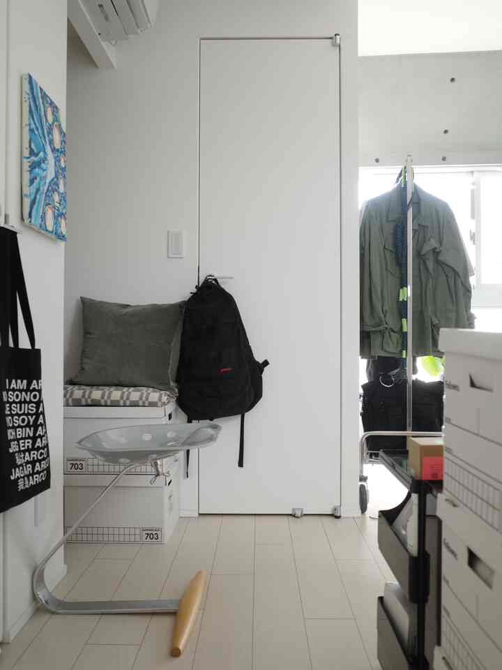 Narrow entryway space in white and green tones, featuring a stool and storage boxes with a tidy interior