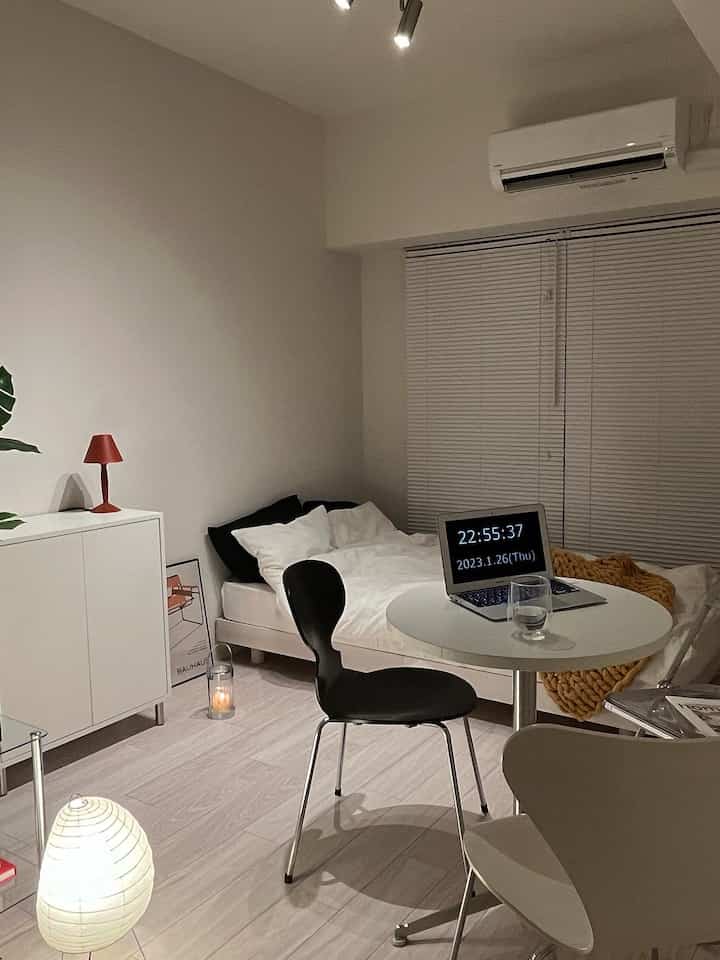白を基調とした一人暮らしの部屋、ベッドと円形のダイニングテーブル、ミニマルな雰囲気のホームオフィス空間