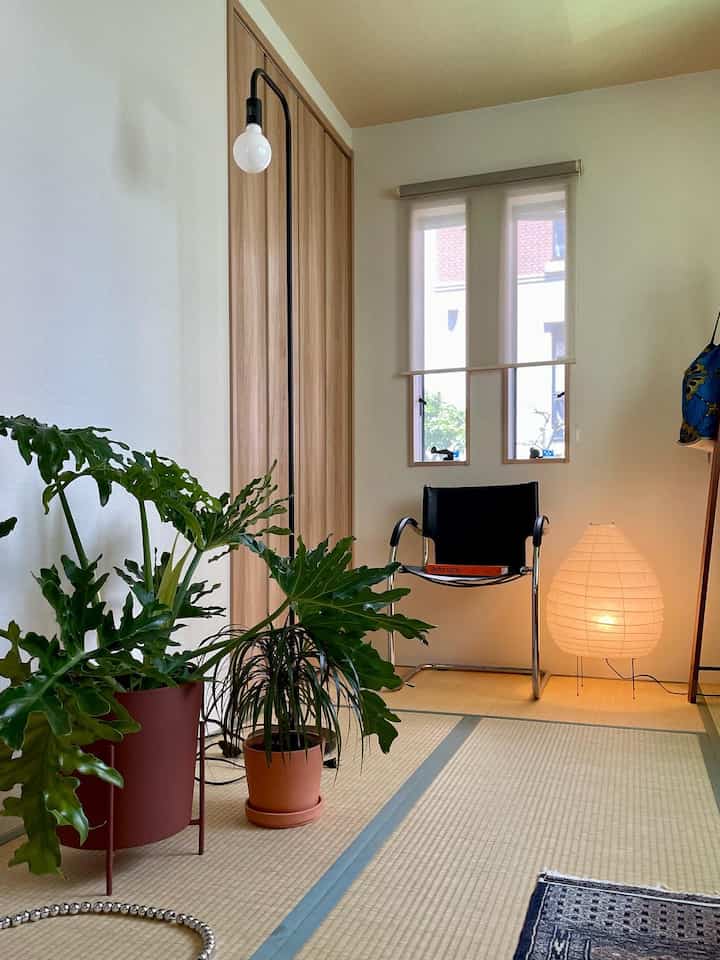 Natural-toned tatami room featuring white walls, floor lamps, and plants with a simple, cozy atmosphere