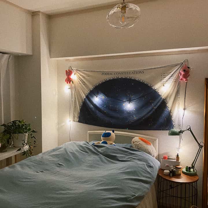 パステル調の寝室、星座のタペストリーとLEDのストリングライトが温かみのある雰囲気を作る居心地の良い空間