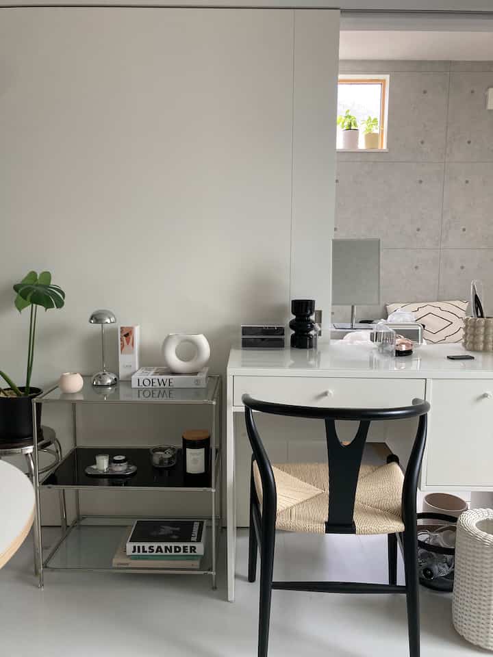 White and black toned powder room featuring a vanity, black chair, and shelf with plant, creating a simple modern space