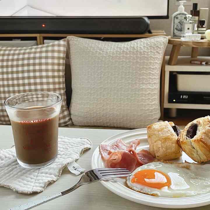 Brown and white toned kitchen space featuring a table with coffee and breakfast, surrounded by cushions in a simple home cafe atmosphere