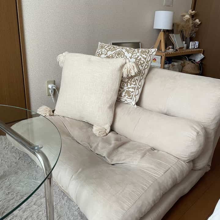 暖かいベージュ色調のリビング、ベージュのソファベッドとクッション、木製のサイドテーブルが配置された落ち着いた雰囲気のインテリア