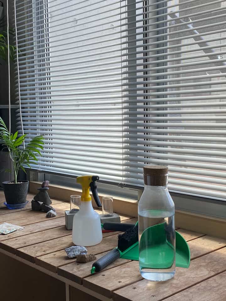 ナチュラルカラーの窓辺、ブラインドがある空間に植物と掃除用具が配置された清潔感のあるインテリア