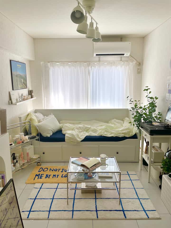 White and blue-toned living and bedroom space featuring a storage daybed and a blue patterned rug with cozy atmosphere