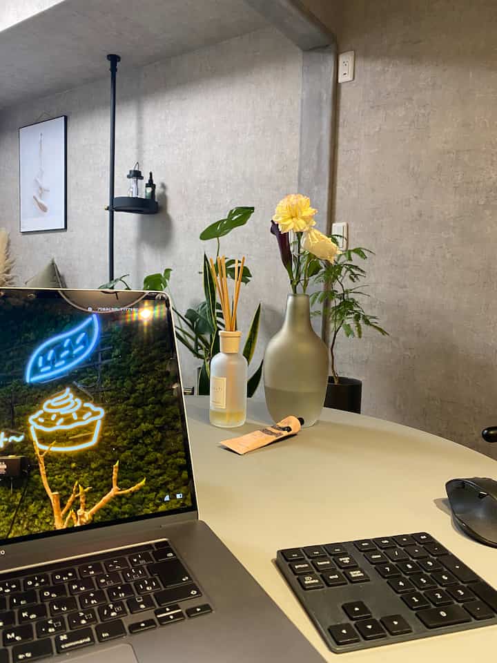 グレーのコンクリート壁紙を背景に、植物とディフューザーを置いたシンプルなホームオフィスの空間