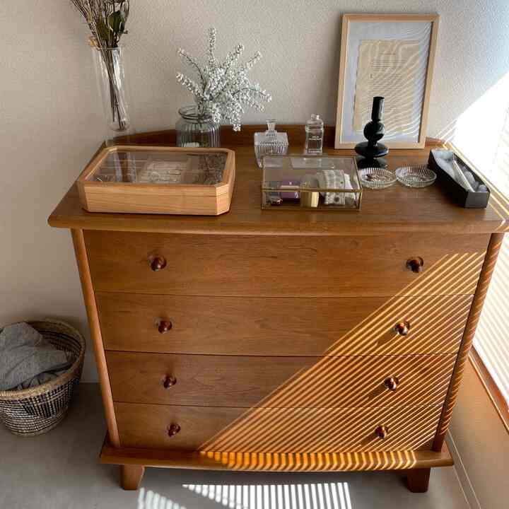 ベージュの壁とブラウンの木製チェストが置かれた、自然光が差し込む雰囲気のある居心地の良い空間