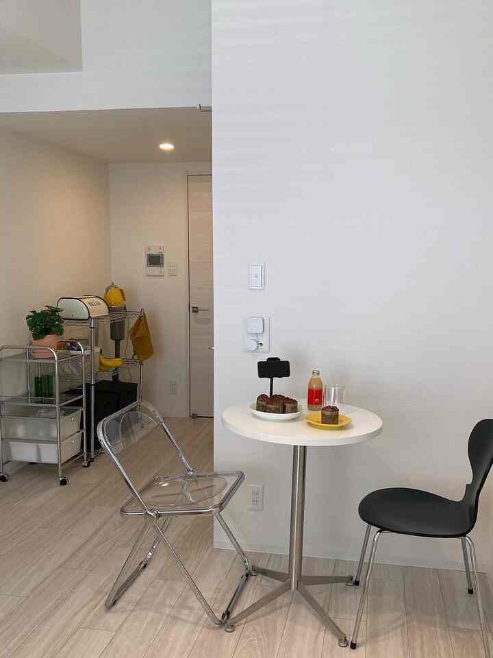 Small dining space in white and transparent tones featuring a clear folding chair, black chair, kitchen cart, and table with plates, creating a clean interior