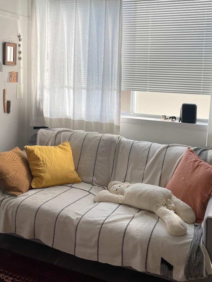 Simple living room sofa space with white tones and yellow cushions, large window allowing natural light creating cozy atmosphere