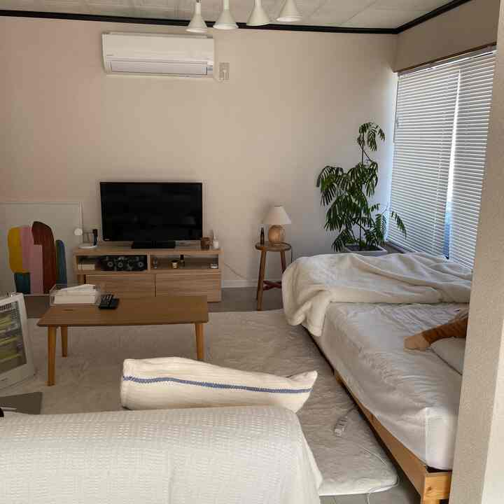 白とベージュの色調の寝室、木製家具とサイドテーブル上のテーブルランプが温かみのある雰囲気を演出している