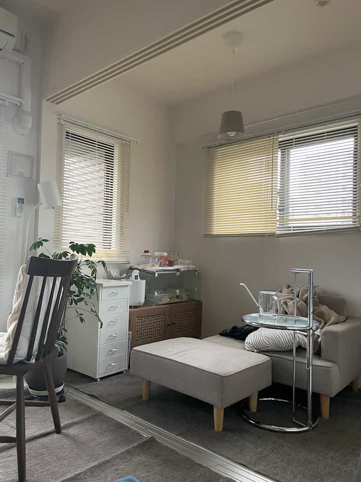 明るくナチュラルなトーンの小さなリビング、コンパクトなソファとブラインドが配置された印象的な空間