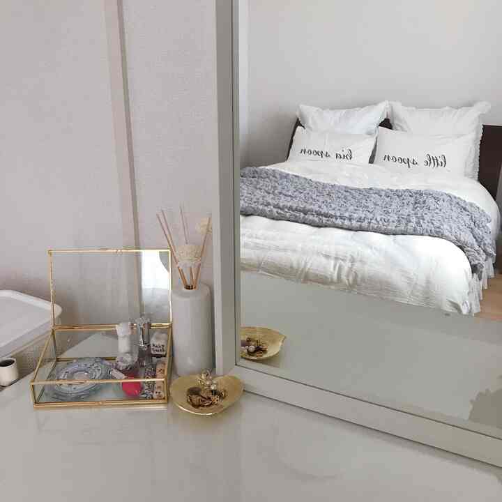 ホワイトとグレーのトーンが特徴の寝室、大きなベッドとクッション、ミニマルな化粧台が配置された印象的な空間