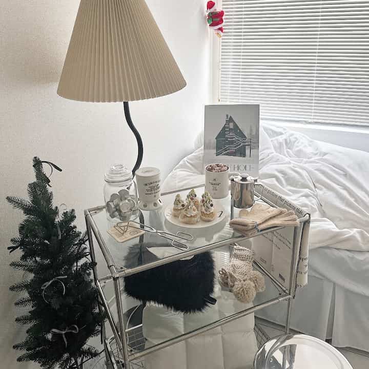 白とベージュのトーンが特徴のワンルーム寝室、強化ガラス3段トロリーとテーブルランプが配置された居心地の良いインテリア