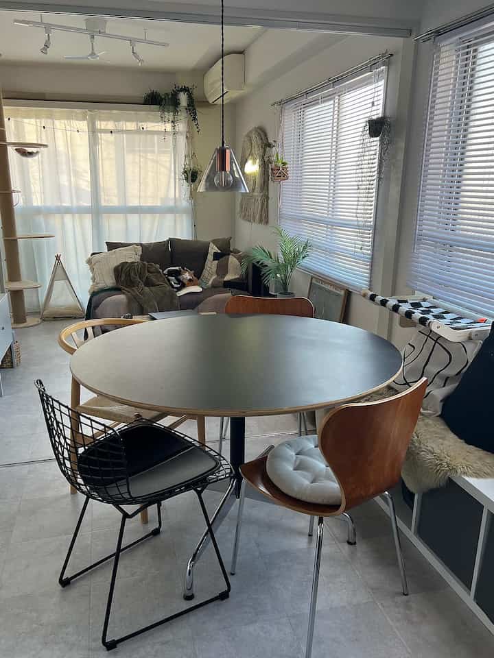 明るいホワイトトーンのダイニング、中央に丸い黒いテーブルと4脚の異なる椅子が配置された雰囲気のある空間