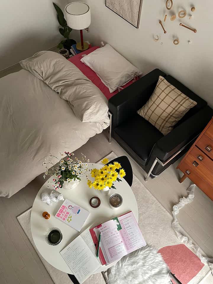 White and yellow toned single household living space with bedroom features, featuring a round table for reading and study alongside a table lamp