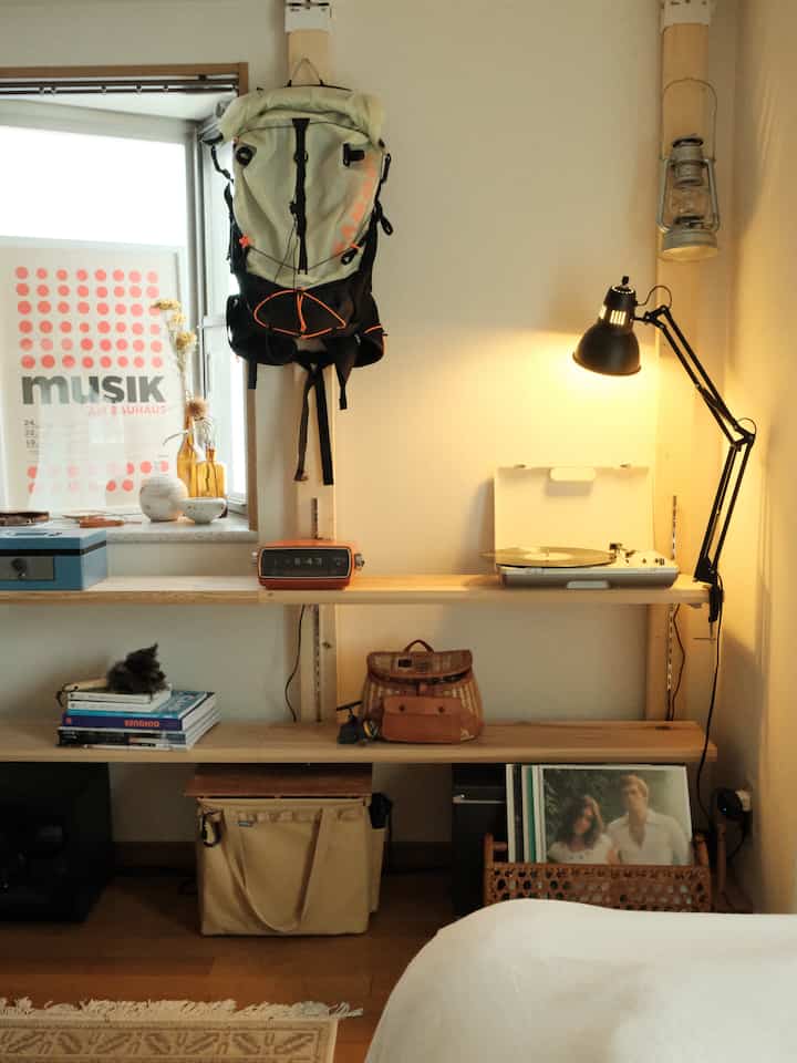 Cozy bedroom with warm wood tones and red accents, featuring vintage audio equipment and illuminated shelving