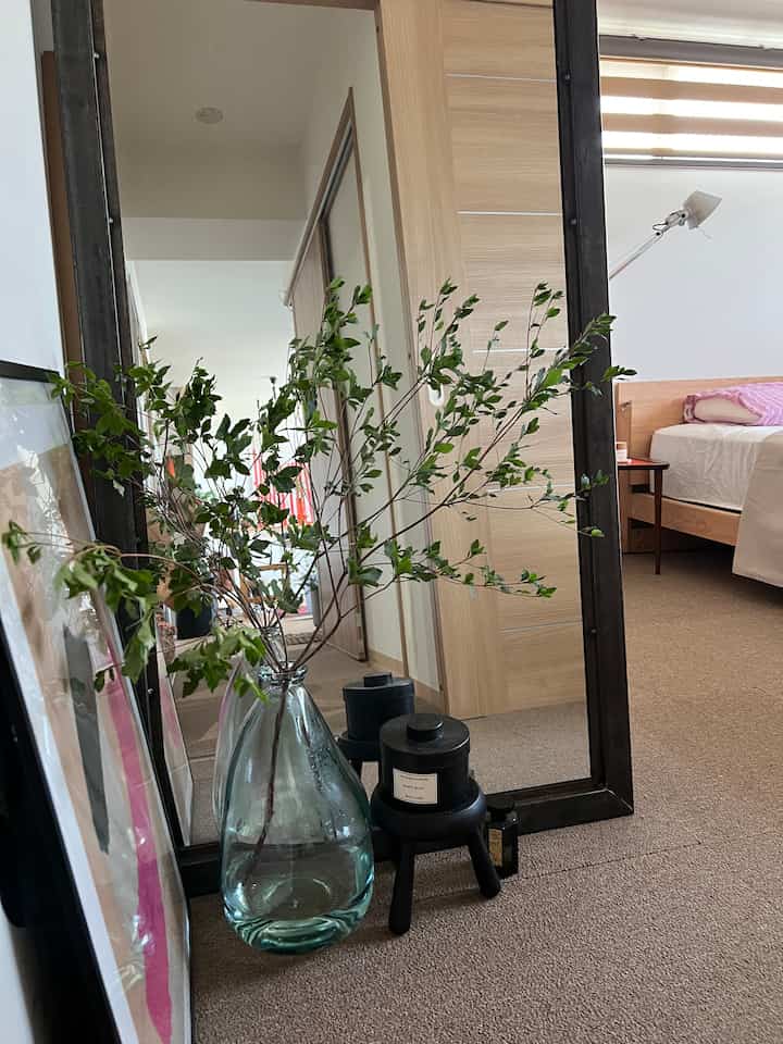 Natural color and wood tone bedroom featuring a large mirror and branch plant in a cozy setting