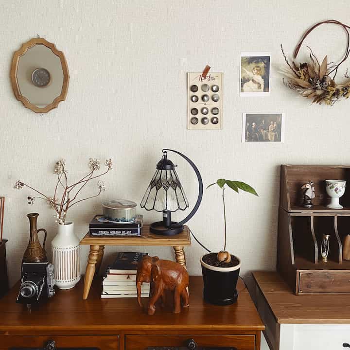 ブラウンとナチュラルカラーのリビングスペース、レトロな家具とヴィンテージ風のテーブルランプ、壁にアートとドライフラワー装飾が配置された雰囲気のあるインテリア