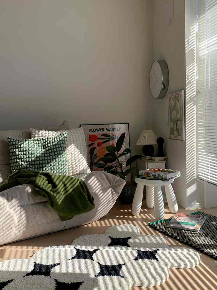 Warm beige and white-toned kitchen-living corner featuring sofa, plants, and blinds casting charming shadows for a cozy atmosphere