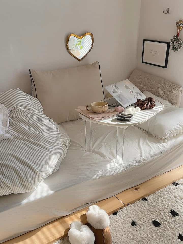 白とベージュの色調のワンルーム寝室、クッションとミニテーブルが配置された居心地の良い読書スペース